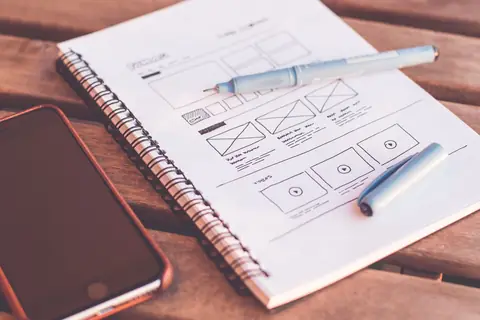Hand-drawn website wireframes in a sketchbook beside a smartphone