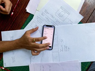 Hand holding a phone over paper sketches of app screens